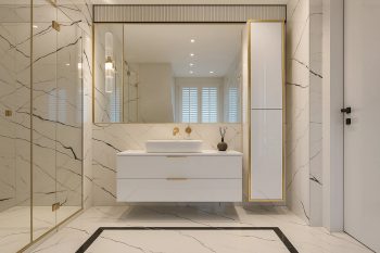 Badschrank Monako im glamourösen Badezimmer mit goldenen Details und großem Spiegel