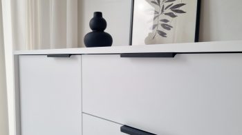 Detailansicht der Kommode Cala Weiß Matt mit schwarzen Griffen und Dekoration