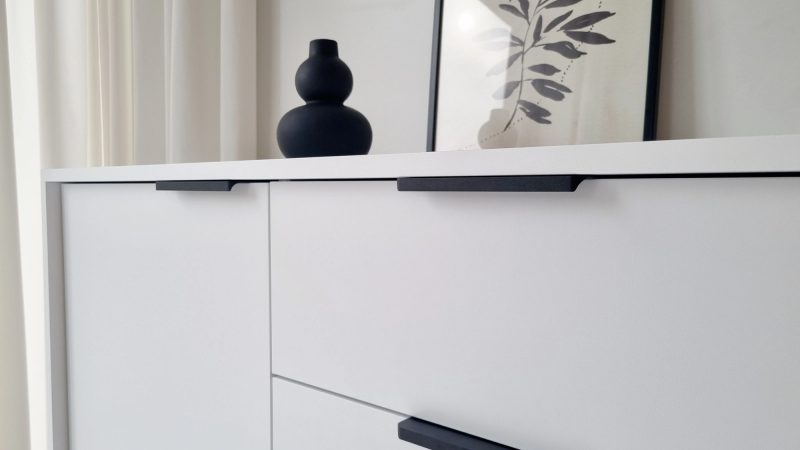 Detailansicht der Kommode Cala Weiß Matt mit schwarzen Griffen und Dekoration