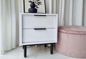 Moderner Nachttisch Cala Weiß – mit rosa Pouf im Hintergrund