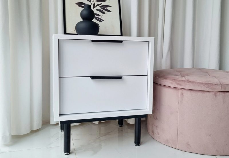 Moderner Nachttisch Cala Weiß – mit rosa Pouf im Hintergrund