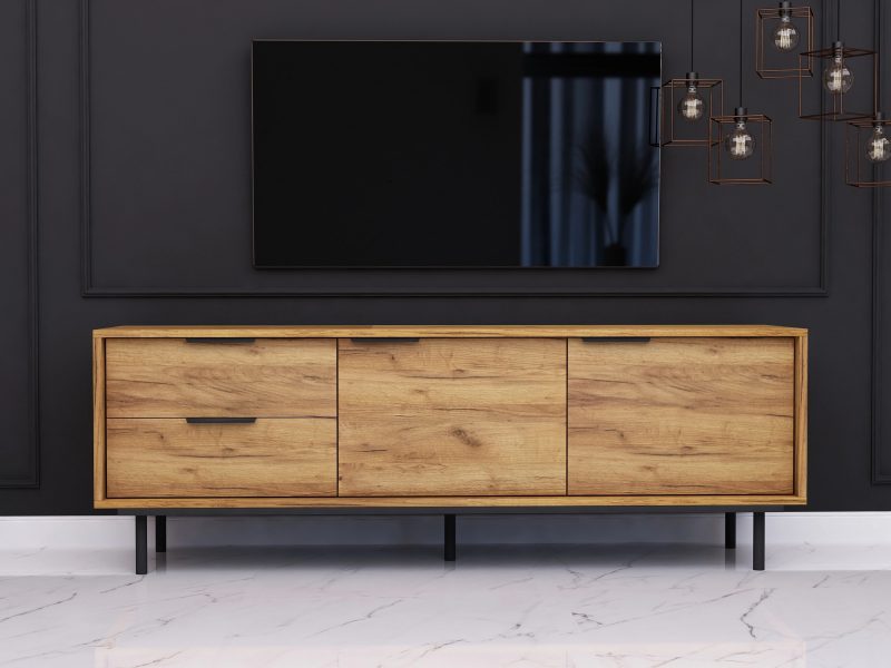 TV-Lowboard Cala 154cm Eiche Craft Gold Matt im Wohnzimmer mit Fernseher an schwarzer Wand.